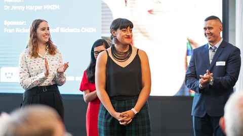 A group of applauding people standing behind Ane Tonga.