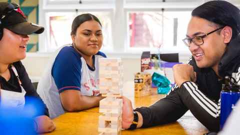 Three people at a table playing a game of Jenga