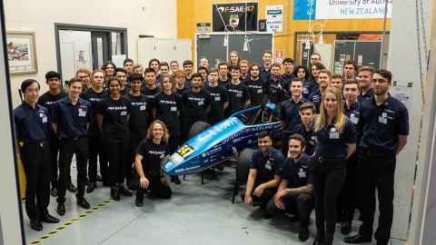 A team of 45 people wearing Formula SAE uniforms gathered around a racing car