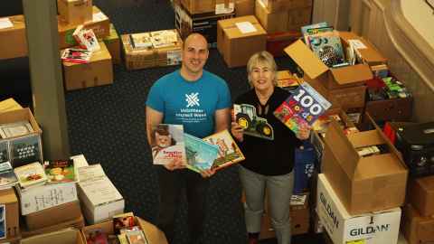 Joel Terwilliger and Cynthia Wallis Barnicoat holding some children's books in a room full of cartons of books.