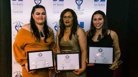 Tamara Thomason-Tata, Tracy Black and Tumanako Bidois holding award certificates and standing in front of a banner with the New Zealand Nurses Organisation logo.