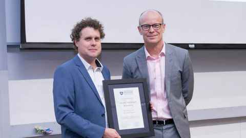 Peter Beck holding a framed certificate, and standing next to Nic Smith.
