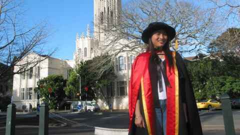 Minh Nguyen wearing academic regalia. The ClockTower is in the background.