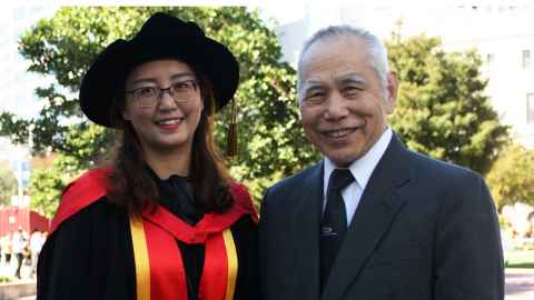 Xiaoqing Li wearing academic regalia and KC Butt wearing a suit and tie.