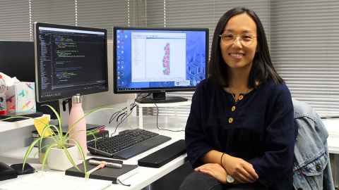 Stephanie Khuu sitting at a desk with a keyboard and two computer monitors.