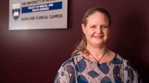 Dr Ngaire Anderson standing next to a sign saying "The University of Auckland School of Medical and Health Sciences, Auckland Clinical Campus."