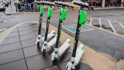 A row of four lime scooters parked beside a carpark.