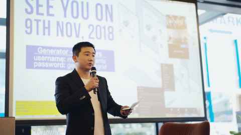 Sam Yin speaking into a microphone in front of a large projector screen