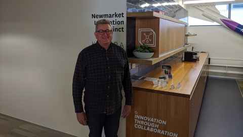 Roger Gower standing at a workspace with "Newmarket Innovation Campus" and "Innovation through collaboration" written on the walls.