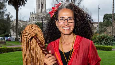 Associate Professor Selina Tusitala Marsh holding a traditional Samoan fue fly whisk, standing in Albert Park with the ClockTower in the background.