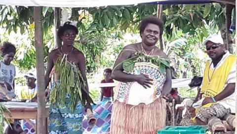 A group of people wearing a mix of traditional and western clothing. Some are holding woven fans with the words "Bougainville Referendum".