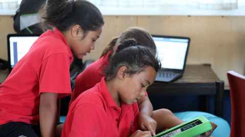 Students wearing red school uniforms working on laptops and tablets