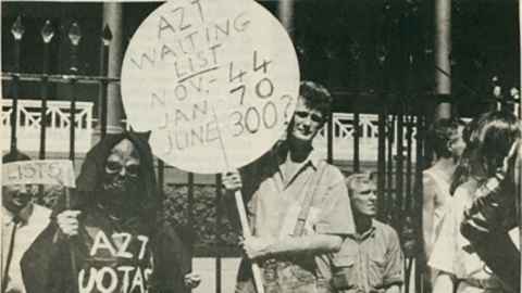 Black-and-white photo of a demonstration with a sign reading "AZT waiting list. Nov 44, Jan 70, June 300?"