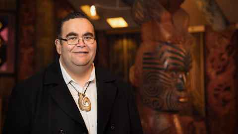 Dr Hirini Kaa standing in front of carvings
