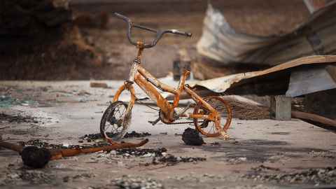 A child's bike burnt by bushfire is pictured amid wreckage of a building: "While they are not trained to identify and help children cope with trauma, they soldier on and do their best," says Professor Mutch of teachers working in disaster-hit communities. Photo: iStock