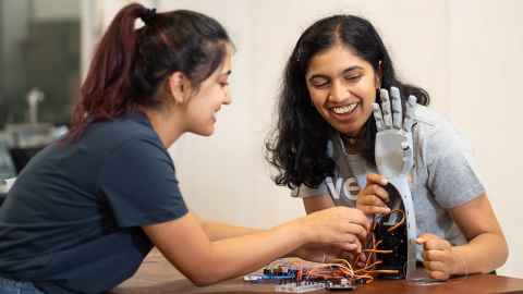 Two young women working on a robotic hand