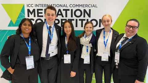 Rima Shenoy, Jacob Siermans, Keeha Oh, Susie McCluskey, Madeleine Tilley and Tunisia Napia wearing lanyards and standing in front of a sign reading "ICC International Commercial Mediation Competition"