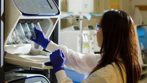 A woman wearing a white lab coat and blue gloves handling lab equipment