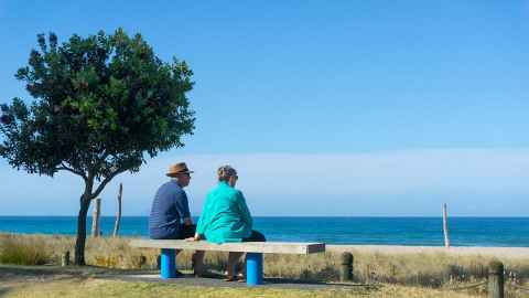 An elderly couple in New Zealand are pictured seated on a bench looking out over the ocean. Last year, NZ Superannuation cost the country $14.5 billion. By 2024 it is projected to cost nearly $20 billion a year. Photo: iStock