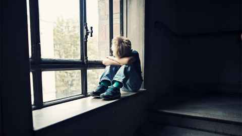 A small child sits alone on a window sill, his head down on his arms: "...a different system is required if we really want to make a difference to the well-being of children," says Ian Hyslop. Photo: iStock