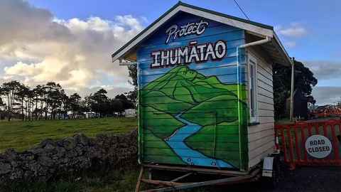 Mural painted on the side of a hut on a trailer. At the top are the words Protect Ihumātao