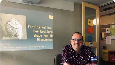 Professor Michael Orsini, in front of a screen displaying the text "Feeling Policy: How Emotions Shape Health Discourses"