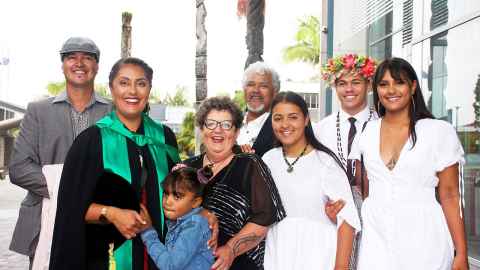 Maia Hetaraka wearing academic regalia, standing alongside her whanau
