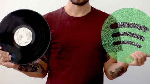 A person holding up a vinyl record in one hand and a large circular Spotify logo in the other hand.