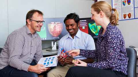 Professor Martyn Nash holding an open book, Dr Prasad Babarenda Gamage holding a model of the heart, and Dr Kat Gilbert pointing to the model