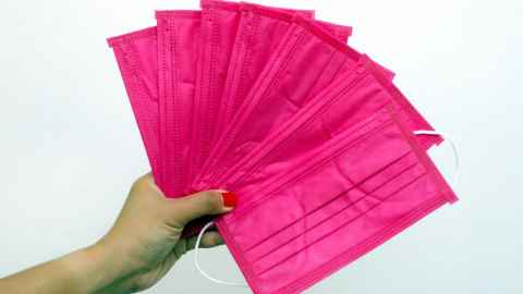 A hand holding seven bright pink facemasks