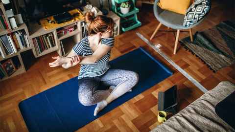 A young woman is pictured practicing yoga alone at home: One of the best ways we know to take care of our brains is to look after our bodies. Photo: iStock