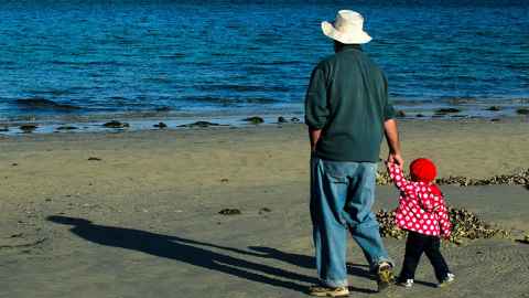The image shows a grandad with a small grandchild hand-in-hand on the beach: The financial pain post-Covid must be fairly shared across the generations. Photo: iStock