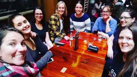 Eight friends sitting around a table with drinks