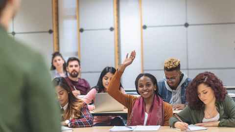 A small class of students looking animated and happy is pictured with the soft focus form of a lecturer on the side of the photo: Without real bodies in a physical classroom, education loses its beating heart. Photo: iStock 