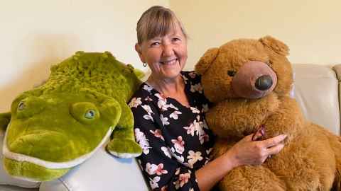 Professor Carol Mutch sitting on a couch with a toy brown bear and green alligator