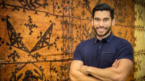 Dr Sam Manuela standing next to a tapa cloth hanging on a wall.