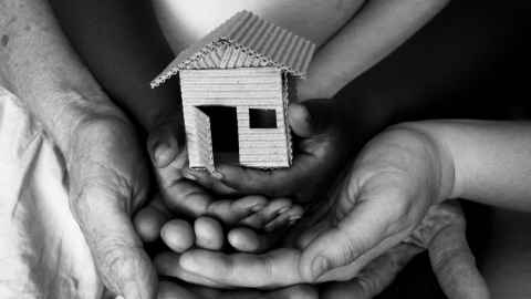 A child's hands holding a model of a house made of corrugated cardboard, with their hands in an adult's hands.