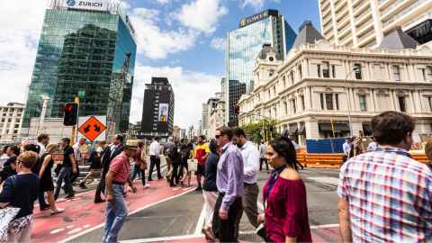 An image shows a crowd of people crossing a busy Auckland street: We need to arrange our cities so the healthy choice is the easy choice, so people can naturally and easily keep their distance, explain Alistair Woodward and Kirsty Wild. Photo: iStock