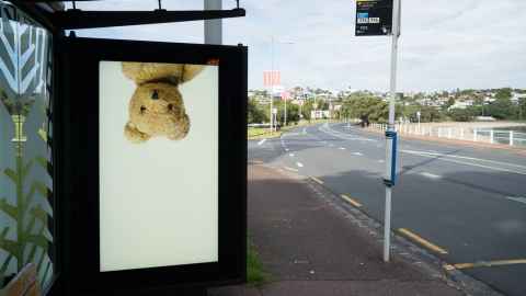 A bus stop with an image of an upside-down teddy bear on the side of the shelter.