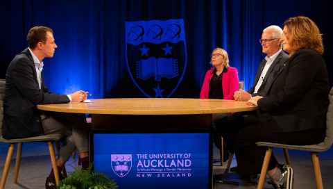 People around a table with the University of Auckland logo behind it.