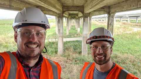 Two men in high vis, under a bridge.