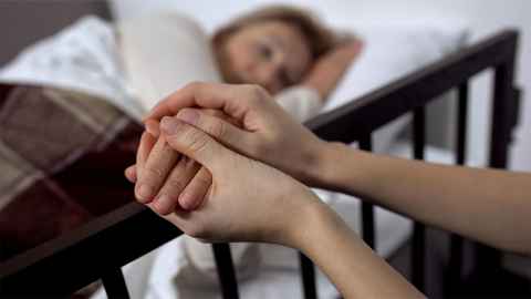 Someone holding a the hand of a patient in a bed.