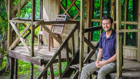 Carl Adams, sitting on the wooden porch of a rustic dwelling.