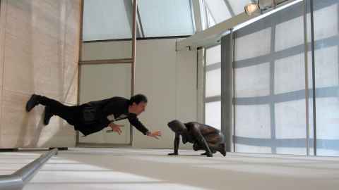 A man apparently hovering over the ground next to a sculpture.
