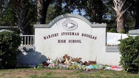A low concrete wall with 'Marjory Stoneman Douglas High School' written on it, and a pile of flowers laid in front.