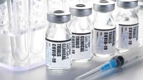 A syringe on a table next to vials with labels that read 'SARS-CoV-2 Clinical Trials Covid-19'.