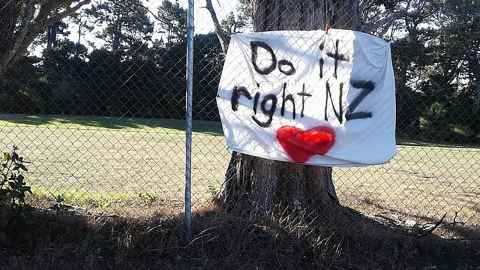 A hand-painted sign stuck to a fence that reads 'Do it right NZ'.