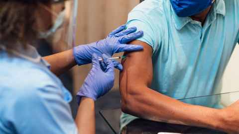The image shows a man in a facemask being vaccinated  by a female health worker: Pacific and Māori people must be prioritised for Covid-19 vaccination. Photo: iStock