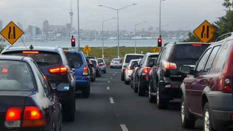 A line of traffic at a North Shore motorway onramp with Auckland City in the background, across the harbour.