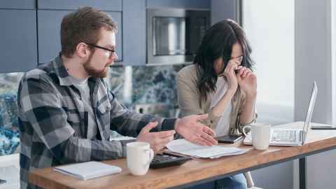 A man and woman with calculator, paper and laptop engaged in a serious discussion.